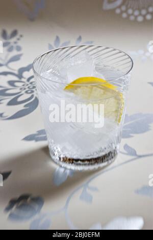 Vetro soffiato a spirale fine di spirito chiaro con soda o tonico, e fetta di limone su sfondo decorativo - Foto Stock