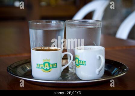 Due piccole tazze di caffè greco con bicchieri d'acqua di accompagnamento serviti in caffè cipriota sulle colline nel sud di Cipro - Foto Stock