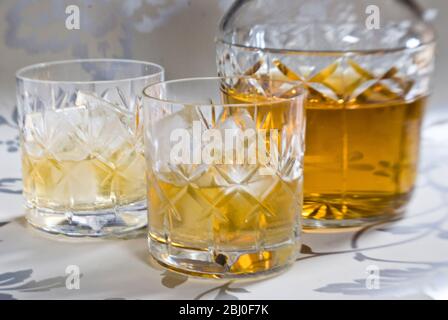 Scotch whisky su ghiaccio in vetro di cristallo di piombo tagliato su superficie decorativa argento, con decanter. - Foto Stock