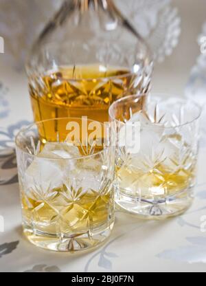 Scotch whisky su ghiaccio in vetro di cristallo di piombo tagliato su superficie decorativa argento, con decanter. - Foto Stock