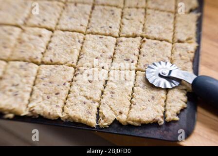 Pasta di biscotto arrotolata su foglio di cottura tagliato con taglierina per pasticceria, prima di entrare in forno - Foto Stock