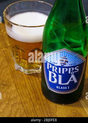 Prips BlÌ´ birra con alcuni versate in un bicchiere su tavolo da ristorante in legno. Si tratta di una birra molto leggera, comunemente bevuta a pranzo o quando il designa Foto Stock