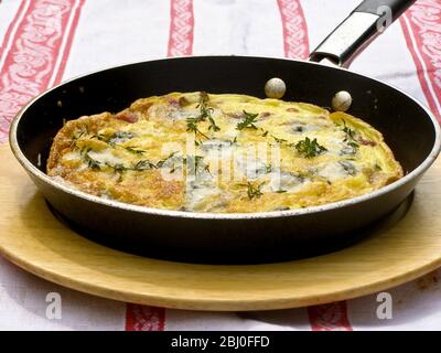 Frittata con formaggio di capra, funghi e timo, servita in padella su piatto di legno. - Foto Stock