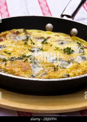 Frittata con formaggio di capra, funghi e timo, servita in padella su piatto di legno. - - Foto Stock