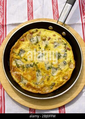Frittata con formaggio di capra, funghi e timo, servita in padella su piatto di legno. - Foto Stock
