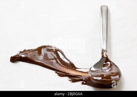 Cioccolato fuso spalmato su superficie bianca con un cucchiaio lasciando una forma a pennacchio. - Foto Stock