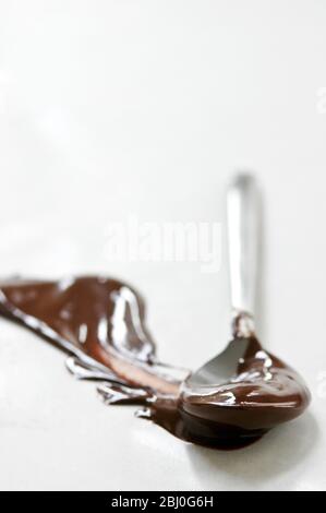 Cioccolato fuso spalmato su superficie bianca con un cucchiaio lasciando una forma a pennacchio. - Foto Stock