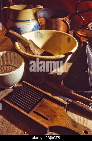 Una collezione di vecchi e antichi kitchenalia, attrezzi e attrezzature tra cui caraffe, ciotole, muffe, setaccio, padelle e bollitore in cina, metallo e rame. - Foto Stock