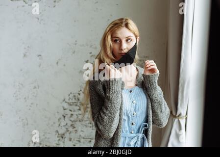 Una ragazza mette una maschera protettiva fatta da sé prima di uscire. Coronavirus pandemico, quarantena, rimanere a casa. Foto Stock