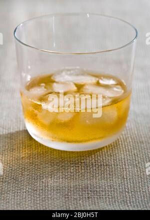Bicchiere di whisky con ghiaccio su tela hessian ruvida - Foto Stock