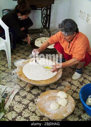 Panettiere donna turca che rotola fuori grandi cerchi sottili di pane su un asse rotondo di legno sul pavimento della panetteria di banchina. Dietro c'è la piastra riscaldante a gas lei Foto Stock