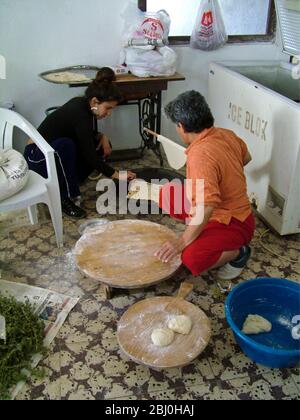 Panettiere donna turca che rotola fuori grandi cerchi sottili di pane su un asse rotondo di legno sul pavimento della panetteria di banchina. Dietro c'è la piastra riscaldante a gas lei Foto Stock