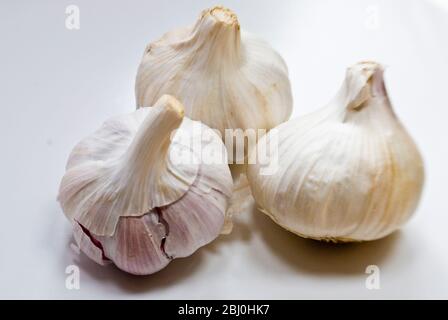 Tre bulbi interi di aglio su superficie bianca - Foto Stock