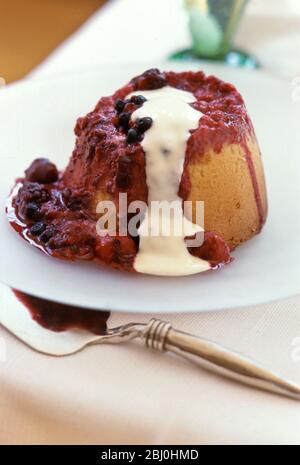 Budino di spugna di marmellata al vapore su piastra bianca, con crema versata sopra - Foto Stock