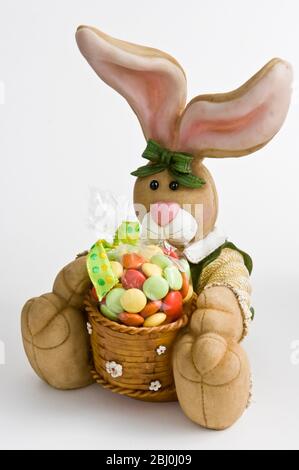 Grazioso ornamento di coniglio con cesto di caramelle come regalo di Pasqua. - Foto Stock