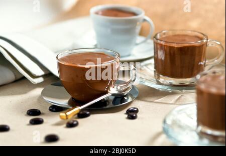 Mousse al cioccolato servita in una varietà di graziose tazze con cioccolatini di chicchi di caffè sparsi intorno al tavolo - Foto Stock