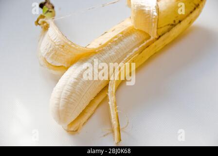 Banana a mezza pelatura su superficie bianca - Foto Stock