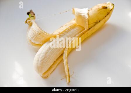 Banana a mezza pelatura su superficie bianca - Foto Stock