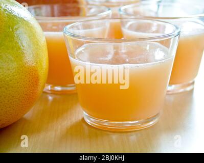 Piccoli bicchieri di succo di pompelmo rosa con pompelmo intero e dimezzato - Foto Stock