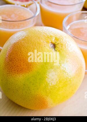 Piccoli bicchieri di succo di pompelmo rosa con pompelmo intero e dimezzato - Foto Stock