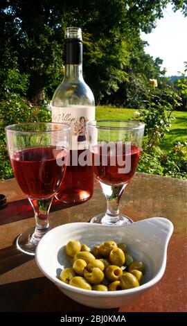 Vino rosato e olive farcite su tavola di ferro arrugginita in giardino di campagna - Foto Stock