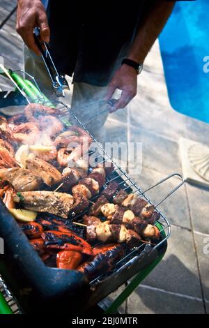 Grigliate di bistecche e bistecche, peperoni rossi, gamberi mediterranei e bistecche di tonno, su una griglia al barbecue a carbone - Foto Stock