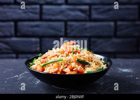 Ciotola nera con riso asiatico fritto con uova strapazzate ai gamberi e cipolle primaverili con salsa tailandese su fondo di cemento scuro davanti al nero Foto Stock