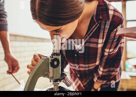 Ragazza che guarda i vetrini in classe biologica attraverso un microscopio. Studente di scuola superiore che studia in una classe di scienza. Foto Stock