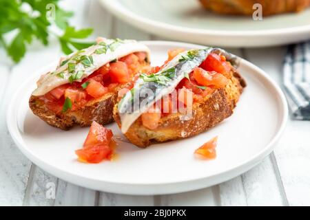 Deliziosa tapa spagnola con acciughe marinate in aceto, pomodoro fresco, olio d'oliva e prezzemolo su fette di pane tostato Foto Stock