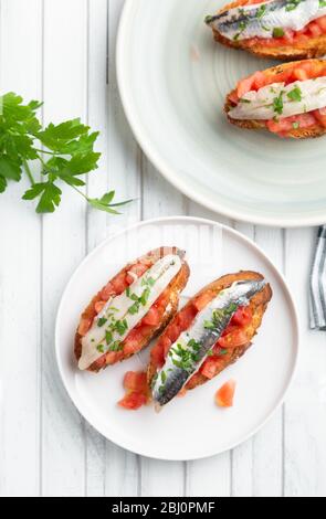 Deliziosa tapa spagnola con acciughe marinate in aceto, pomodoro fresco, olio d'oliva e prezzemolo su fette di pane tostato Foto Stock
