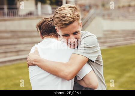 Due ragazzi si abbracciano l'un l'altro nel campus universitario. Gli studenti delle scuole superiori sorridono e si danno un abbraccio all'aperto. Foto Stock