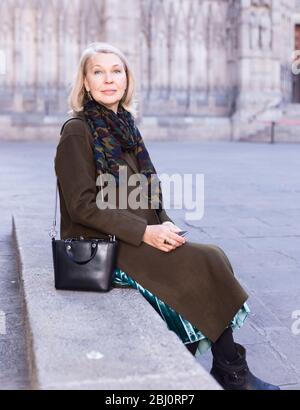 Positivo donna matura si siede sulla scalinata di pietra nella città vecchia Foto Stock