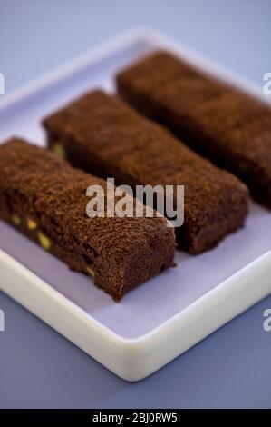 Tre fette di torta di vassoio di cioccolato spolverate con polvere di cacao su piatto di mauve quadrato - Foto Stock