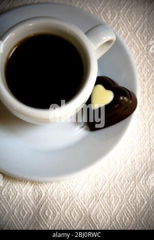 Cioccolato a forma di cuore su piattino di piccola tazza di caffè nero - Foto Stock