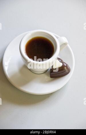 Cioccolato a forma di cuore su piattino di piccola tazza di caffè nero - Foto Stock