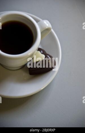 Cioccolato a forma di cuore su piattino di piccola tazza di caffè nero - Foto Stock