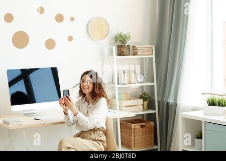 Scatto orizzontale di giovane allegra donna con capelli ricci che parla al telefono utilizzando l'app per videochiamate Foto Stock