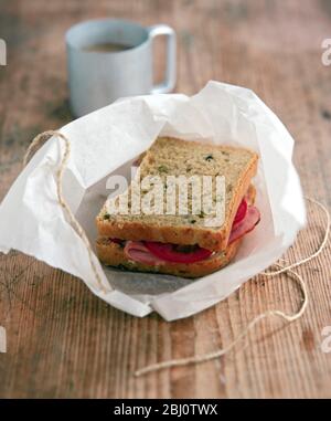 Panino di pane marrone con pomodoro e prosciutto non avvolto da pacco di carta avvolta legata con corda - Foto Stock