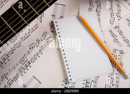 Scena di registrazione musicale con chitarra e memo pad su sottofondo di fogli musicali Foto Stock