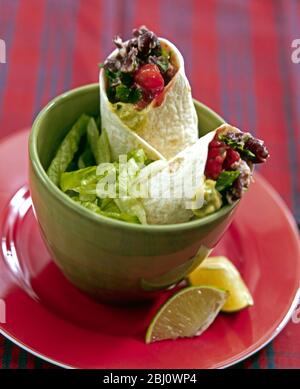 Pranzo leggero di miscela di chili avvolta in tortillas molle con insalata e cunei di limone in ciotola verde - Foto Stock