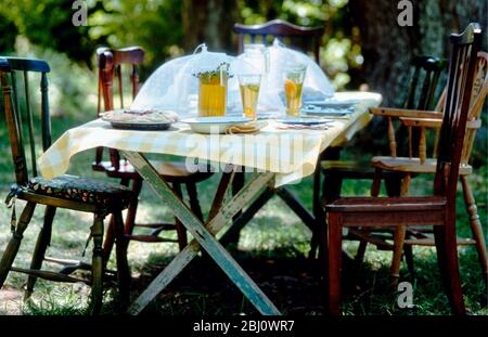 Comodo tavolo e sedie vecchio set fuori sotto un albero al sole per un pasto picnic - Foto Stock