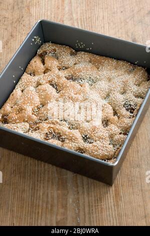 Torta di semola con fichi e sesamo ancora nel suo vassoio quadrato sul tavolo da cucina - Foto Stock
