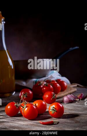 Pomodori ciliegini su vecchio tavolo di legno con aglio, pepe caldo e olio Foto Stock