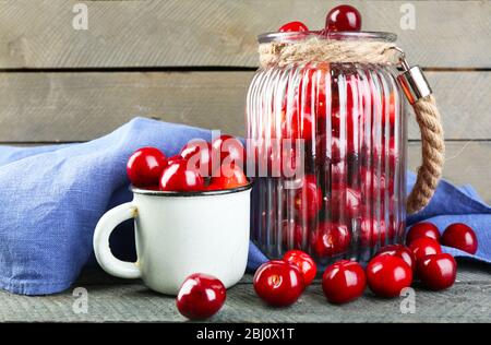 Ciliegie dolci in vaso di vetro e tazza, su sfondo legno Foto Stock