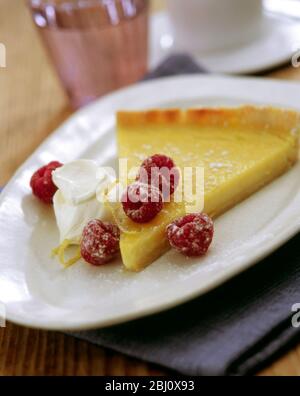 Fetta di classica crostata di limone servita con lamponi freschi, scorza di limone e creme fraiche - Foto Stock