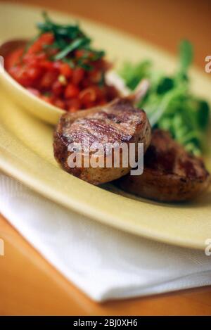 Costolette di agnello alla griglia con salsa di pomodoro e insalata su piatto di glassa di crackle giallo - Foto Stock