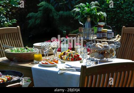 Elegante barbecue tavolo pranzo fuori al sole, insalata in grande ciotola di legno, insalata di pomodoro e mozzarella, kebab di verdure, condimento olio d'oliva, pane r Foto Stock