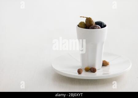 Olive italiane miste in alto vaso bianco in ceramica su piatto bianco con pietre su fondo bianco - Foto Stock