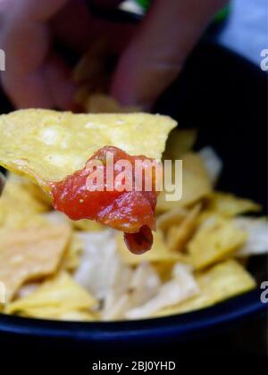 Tortilla chip immerso in salsa con più chip in background - Foto Stock