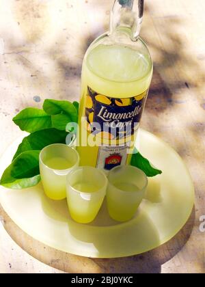Bottiglia di limoncello liquore con tre bicchieri e foglie di limone - Foto Stock